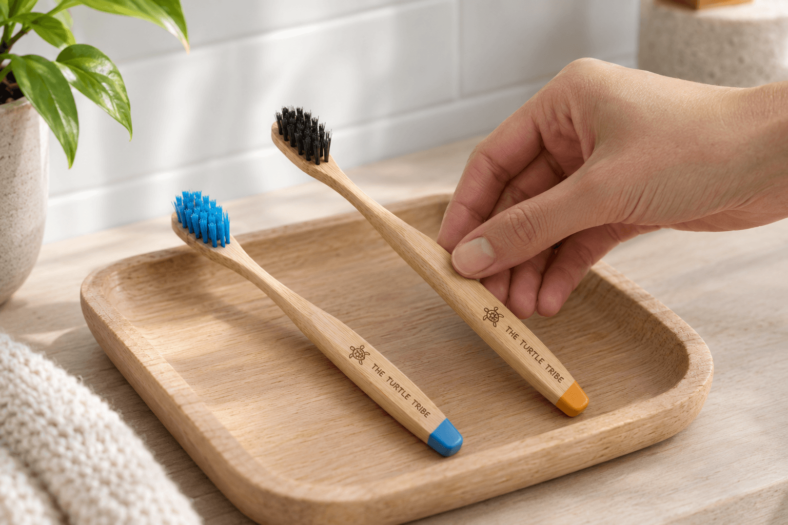 Two The Turtle Tribe bamboo toothbrushes on a wooden tray, one with blue nylon bristles and one with black natural bristles