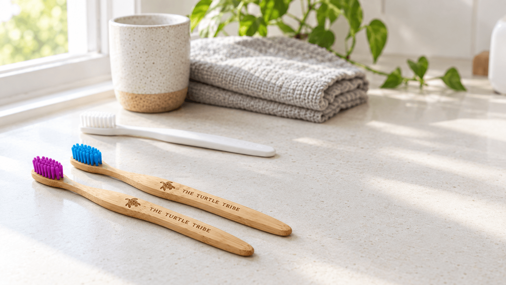 Two The Turtle Tribe bamboo toothbrushes with nylon bristles on a bathroom bench, with a plain plastic toothbrush behind them